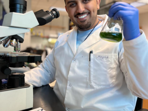 Majeed in the lab, holding up a beaker with algae