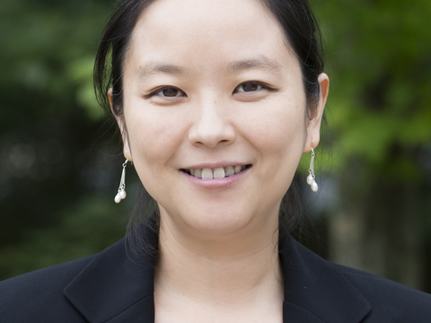 Head shot of Xin Zhang with green leaves in background. 