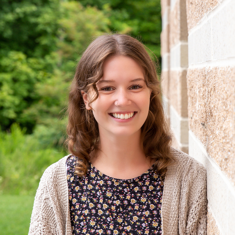 Sarah Endyke headshot, outside, leaning against stone wall of Appalachian Lab with trees in background. 