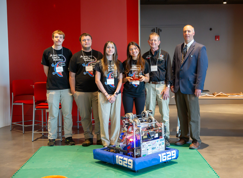 four GaCo students in uniform of black shirts and tan slacks pictured with award and Chuck Trautwein and David Nelson. Robot is in foreground with red wall in background.  