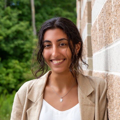 Headshot of Nicole Ibrahim, outside, leaning against stone wall of the Appalachian Laboratory with trees in background. 